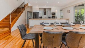 A modern kitchen with a central island, a dining area with a wooden table and chairs, and a staircase leading to an upper level.