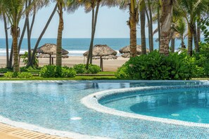A swimming pool with a curved edge, surrounded by palm trees and a beach view. - Luxury Condo with Private Beach 4BR (Acapulco)