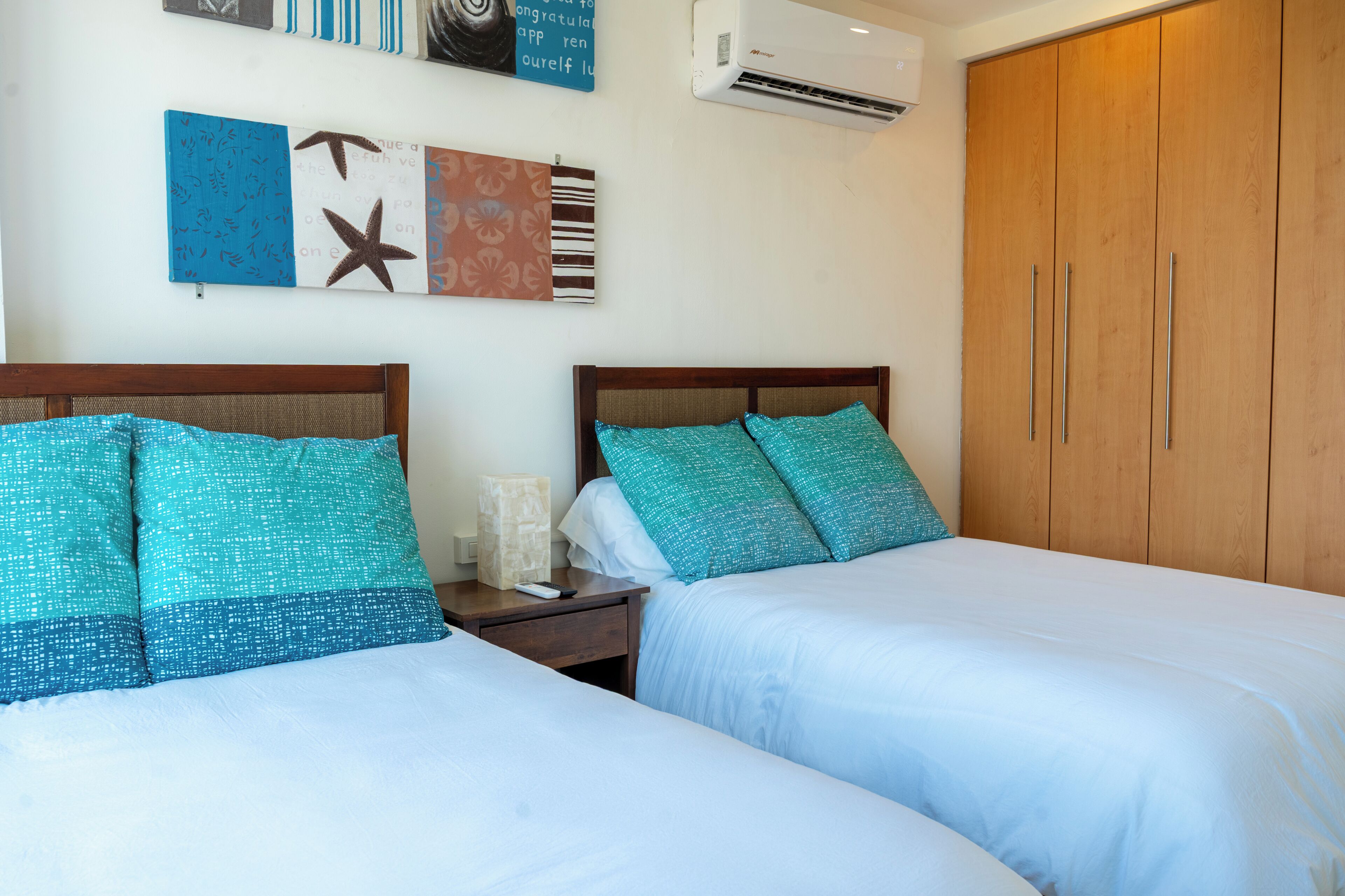 A hotel room with two beds, a nightstand, a wall-mounted air conditioner, and a wooden wardrobe.
