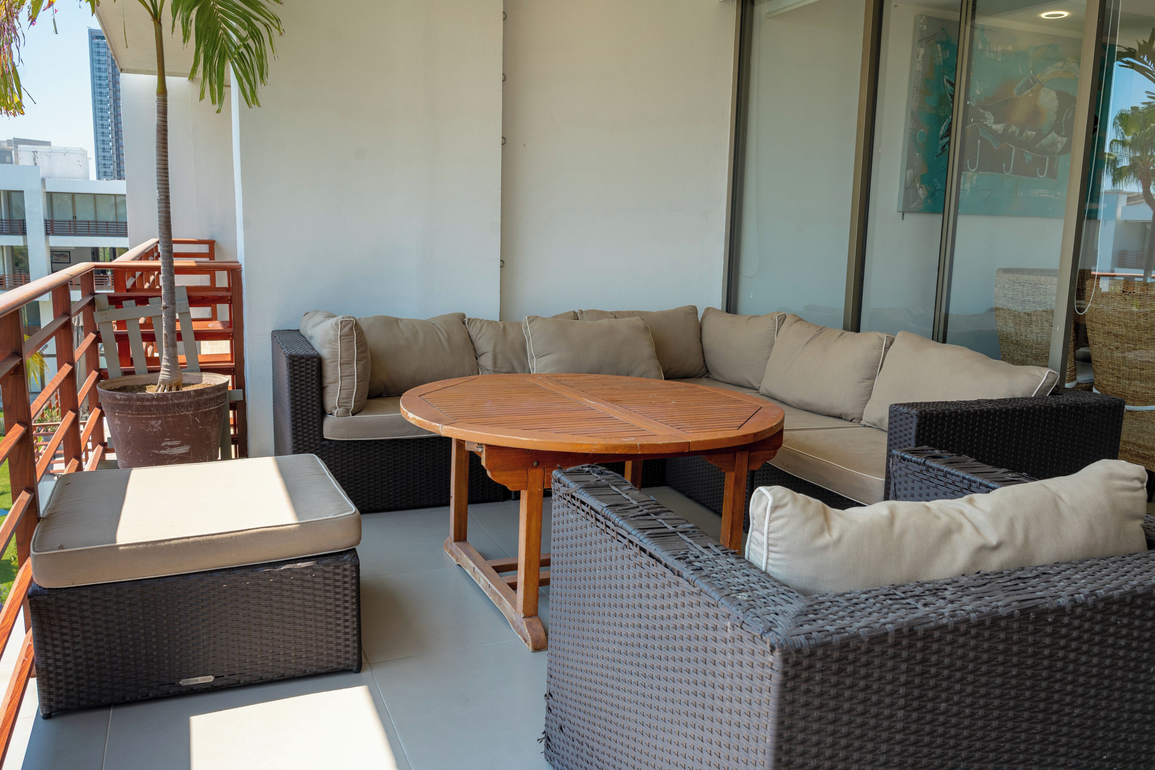 Un balcon avec un canapé, une table ronde, des meubles en osier et une plante en pot.