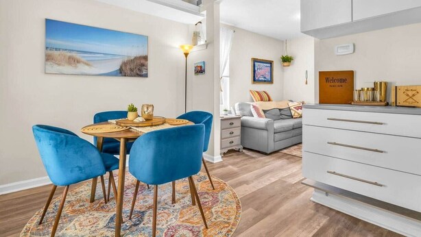 En moderne stue med spiseplads, en grå sofa, et hvidt skab med guldgreb, og et billede af en strand.