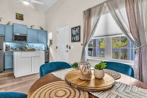 Eine moderne Küche mit blauen Schränken, einem Esstisch mit blauen Stühlen und einem großen Fenster mit Vorhängen.