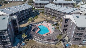 A multi-story hotel with a central courtyard featuring a swimming pool, surrounded by balconies and a small garden area. - Tilghman Beach & Racquet Club 224 (North Myrtle Beach)