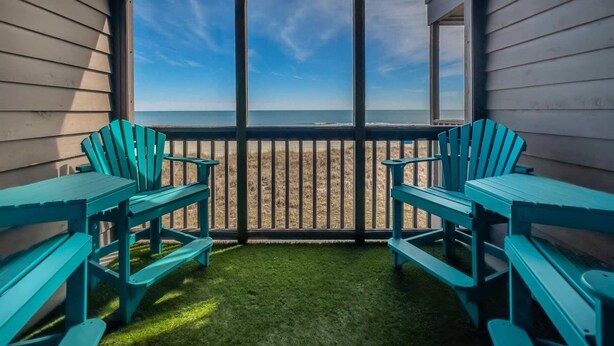 A covered outdoor area with a view of the beach, featuring two turquoise chairs and a table. - Tilghman Beach & Racquet Club 224 (North Myrtle Beach)