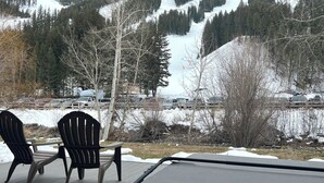 Une terrasse avec deux fauteuils Adirondack et un jacuzzi, offrant une vue sur un paysage montagneux enneigé.