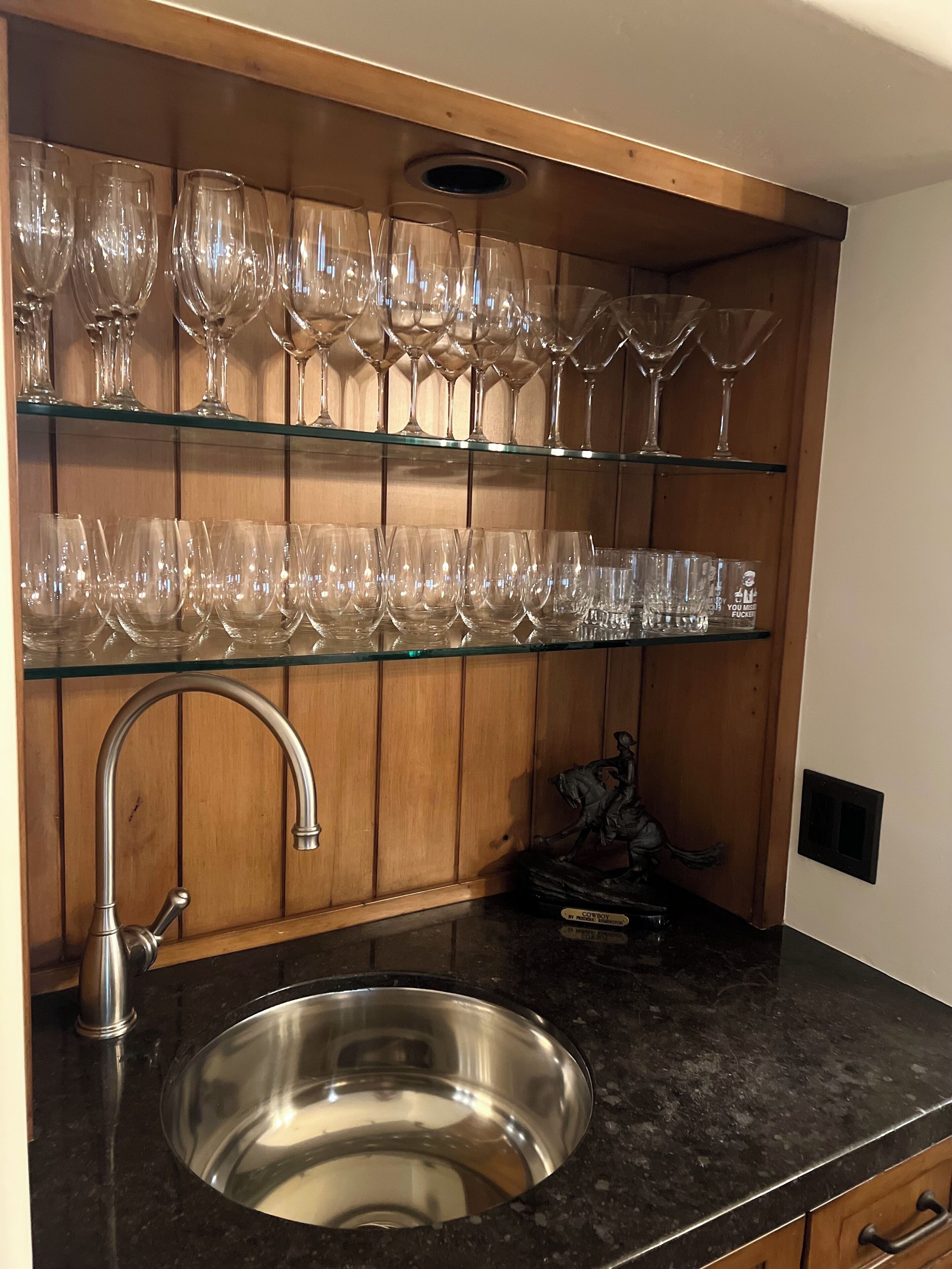 A kitchen with a stainless steel sink, wooden cabinets, and multiple wine glasses on shelves.