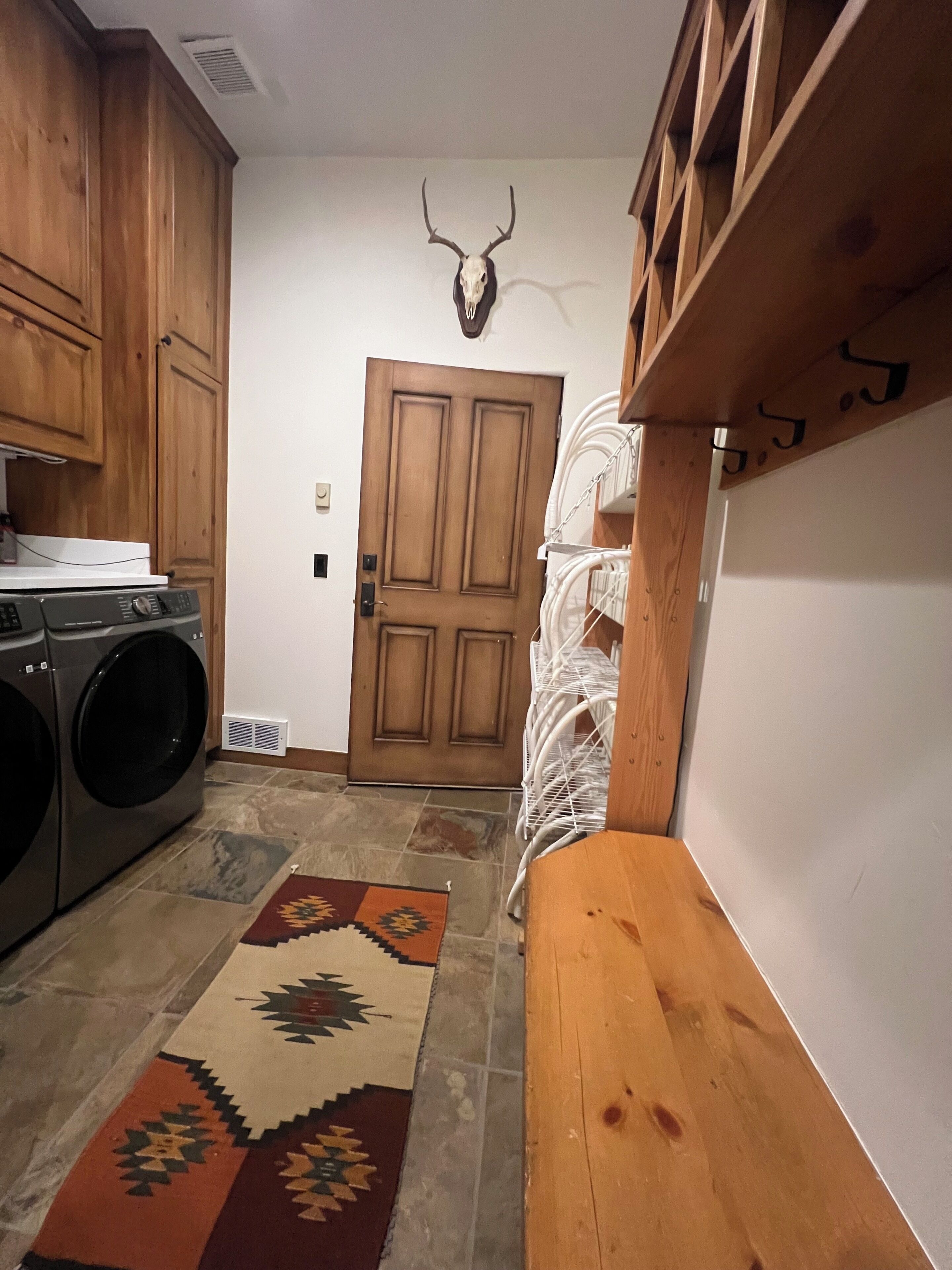 A kitchen with wooden cabinets, a washing machine, a patterned rug, and a deer skull on the wall.