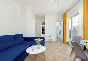 Ein modernes Wohnzimmer mit einem blauen Sofa, einem kleinen weißen Tisch mit einer Blumenvase und einem grauen Sessel.