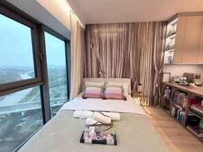 A bedroom with a large window, a bed with multiple pillows, a bedside table with a lamp, and a bookshelf. - Subtelna Elegancja Olszynki Park (Rzesz ów)