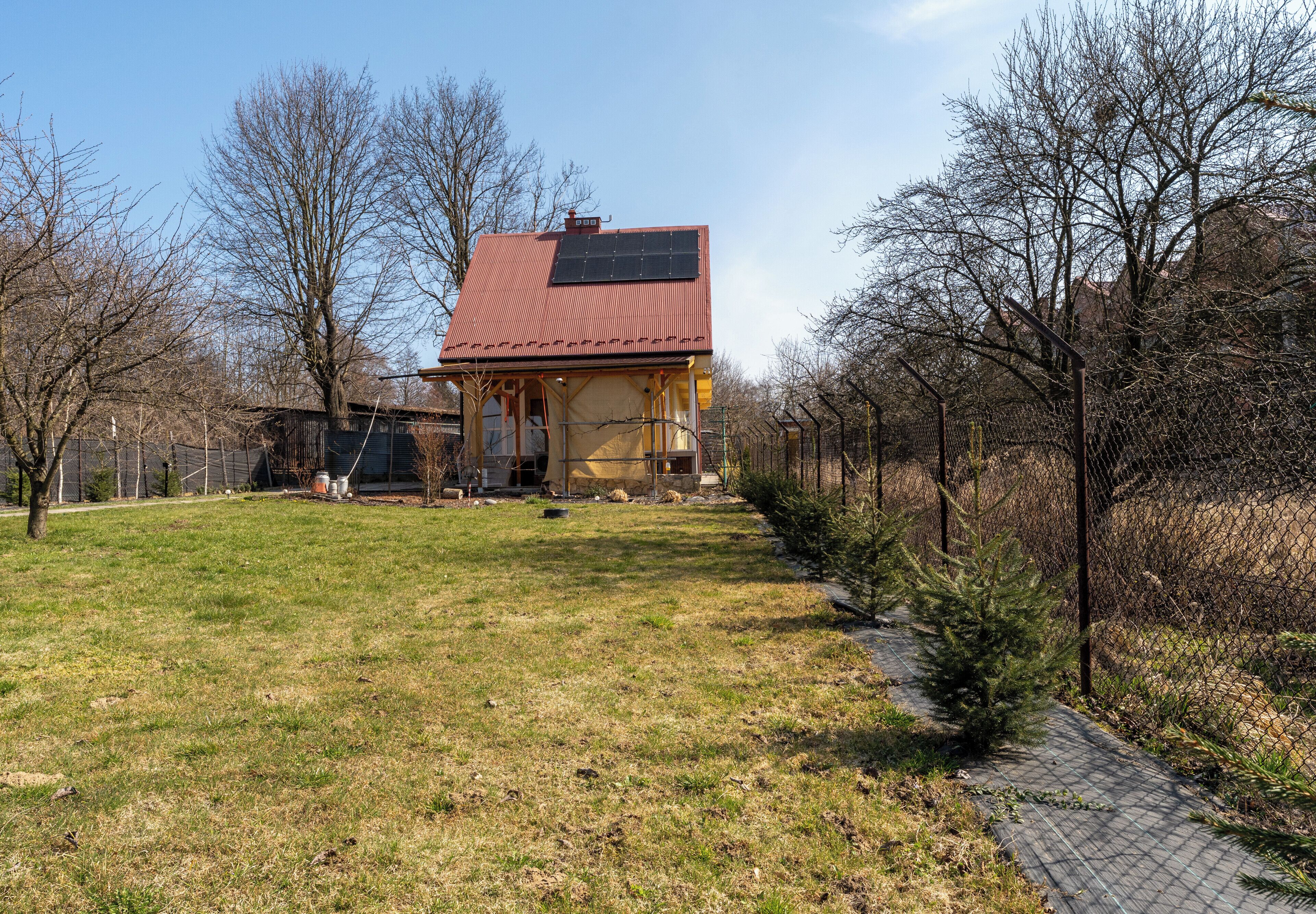 Una casa con techo rojo, paneles solares y un patio cercado.
