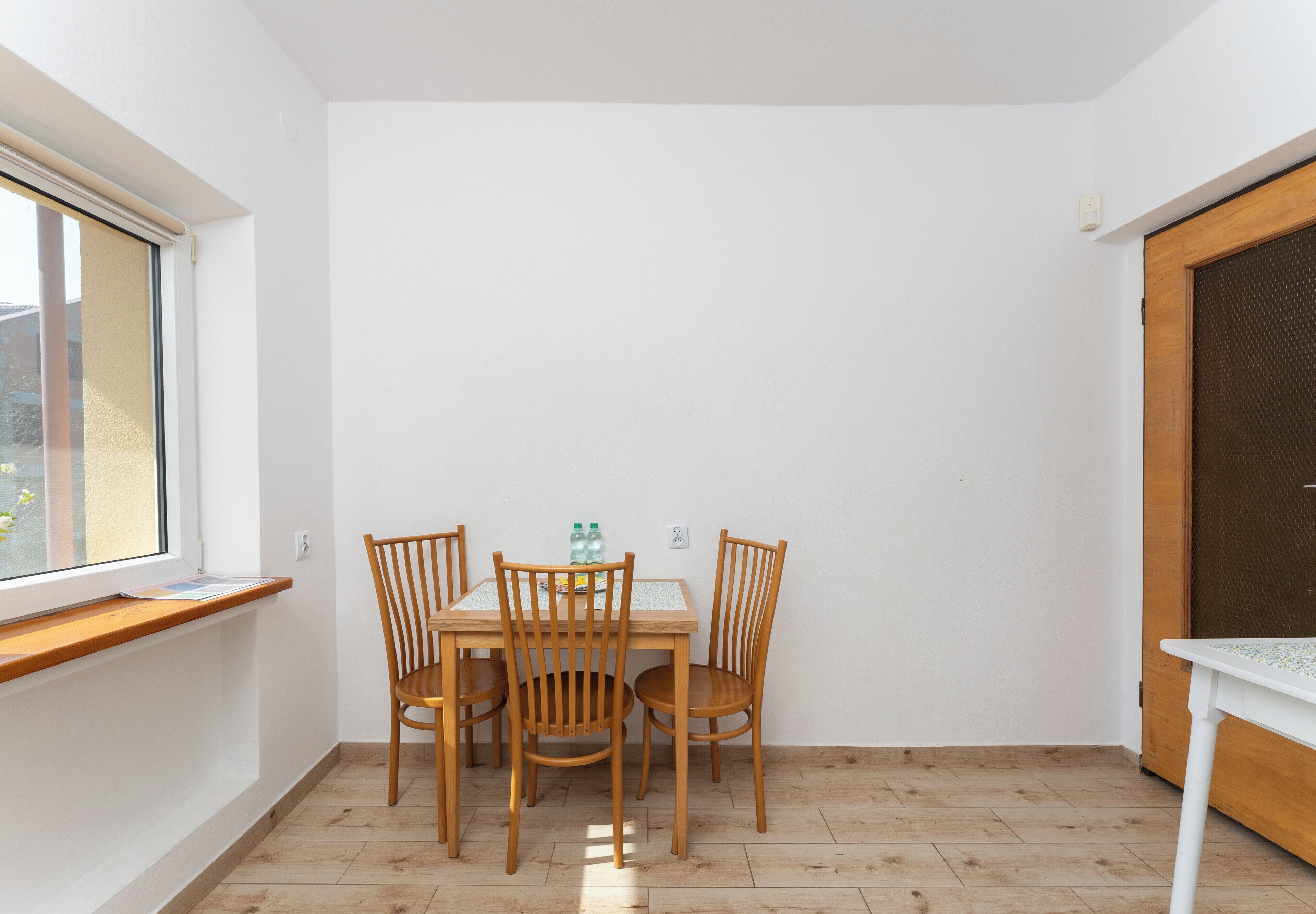 A corner room with a dining table, four chairs, a window, and a door.