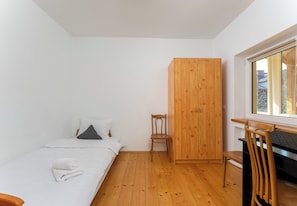 Un dormitorio con una cama, un armario de madera, una silla y un escritorio cerca de una ventana.