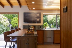 A modern kitchen with a dining area, wooden cabinets, a built-in oven, and a large window. - The Art House | Queenstown lakefront & central location (Queenstown)