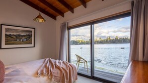 A bedroom with a large window, a bed, a chair, and a painting on the wall. - The Art House | Queenstown lakefront & central location (Queenstown)