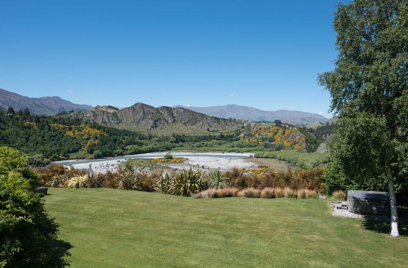 A grassy area with a river, mountains, and trees.