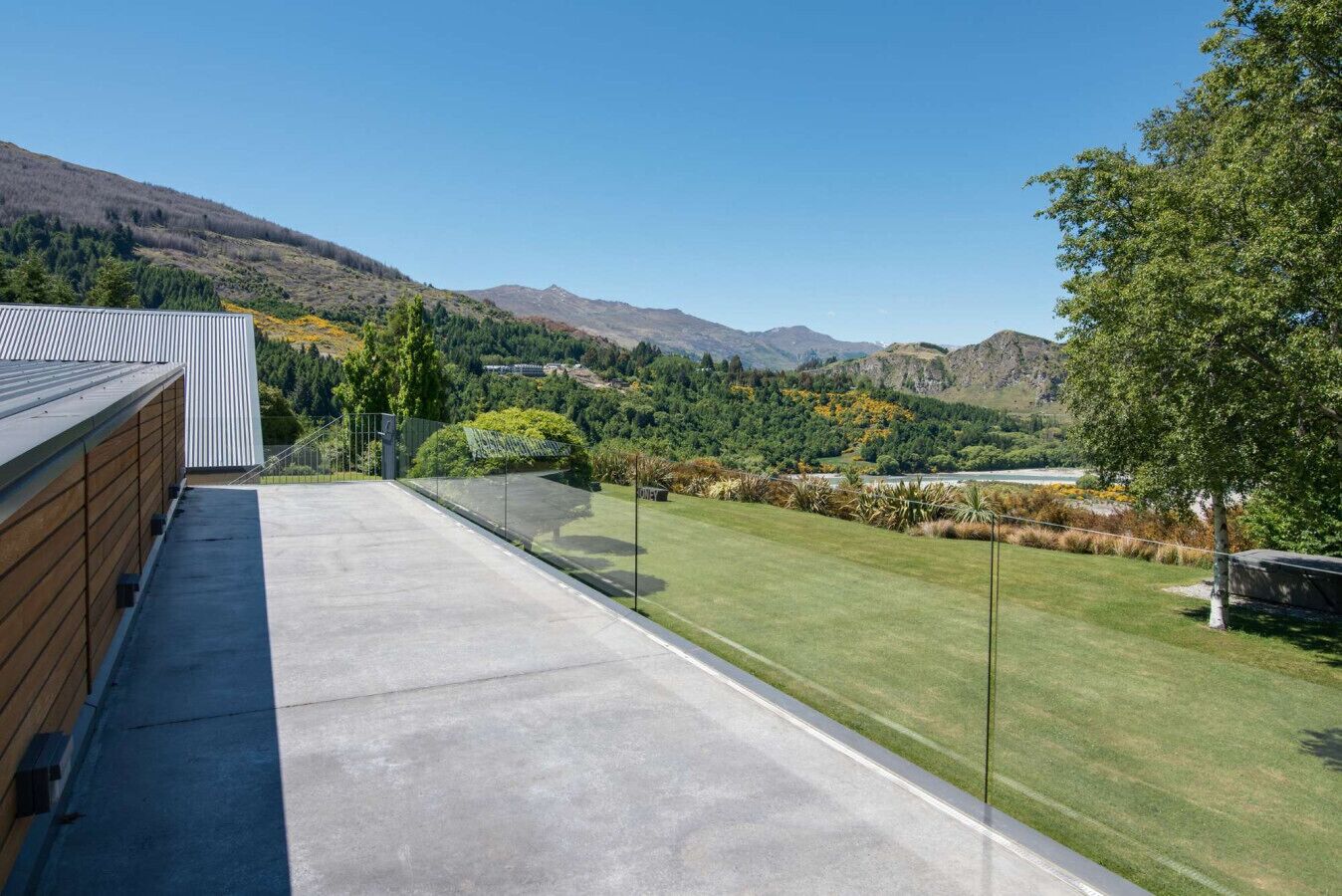 A rooftop terrace with a view of a mountainous landscape, a grassy lawn, and a wooden building structure.