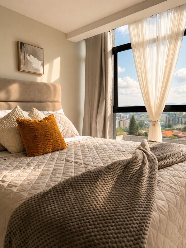 Une chambre à coucher avec un lit, des oreillers, une couverture, une fenêtre avec des rideaux et un tableau au mur.
