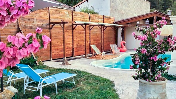 Een achtertuin met een zwembad, twee ligstoelen, een houten schutting en een flamingo decoratie.