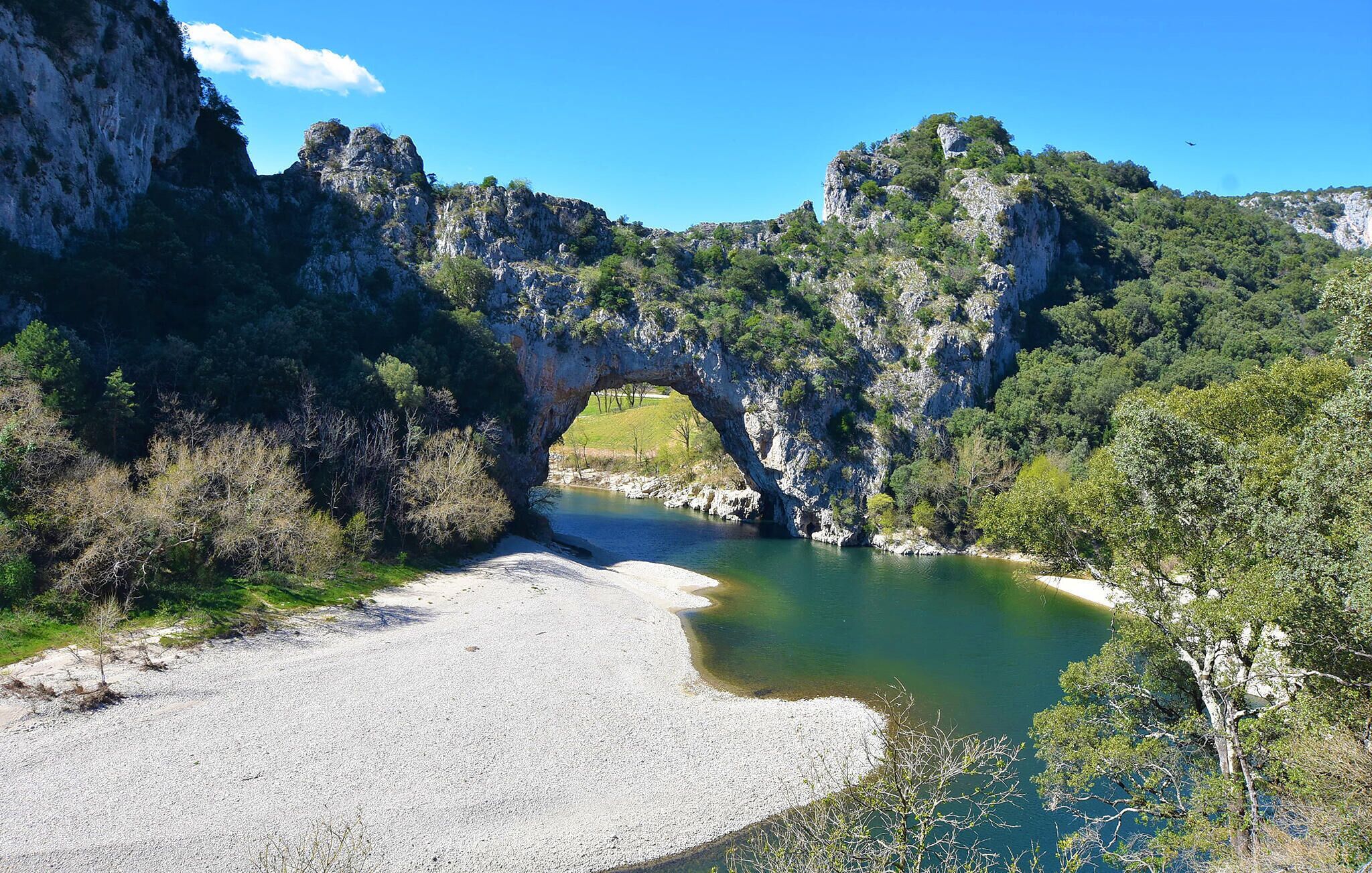 A natural rock arch over a river, surrounded by greenery and rocky cliffs.
