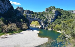 Ein natürlicher Felsbogen über einem Fluss, umgeben von Grün und felsigen Klippen.