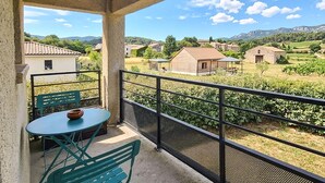 Een balkon met een tafel en stoelen, met uitzicht op een wijngaard en huizen in een landelijke omgeving.