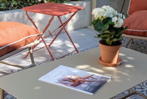 A table with a magazine, a potted plant, and orange cushions. - Studio with Garden – Cannes City Centre (Cannes)
