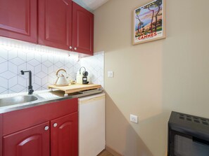 A kitchen with red cabinets, a white dishwasher, a kettle, and a coffee maker on a wooden countertop. - Studio with Garden – Cannes City Centre (Cannes)