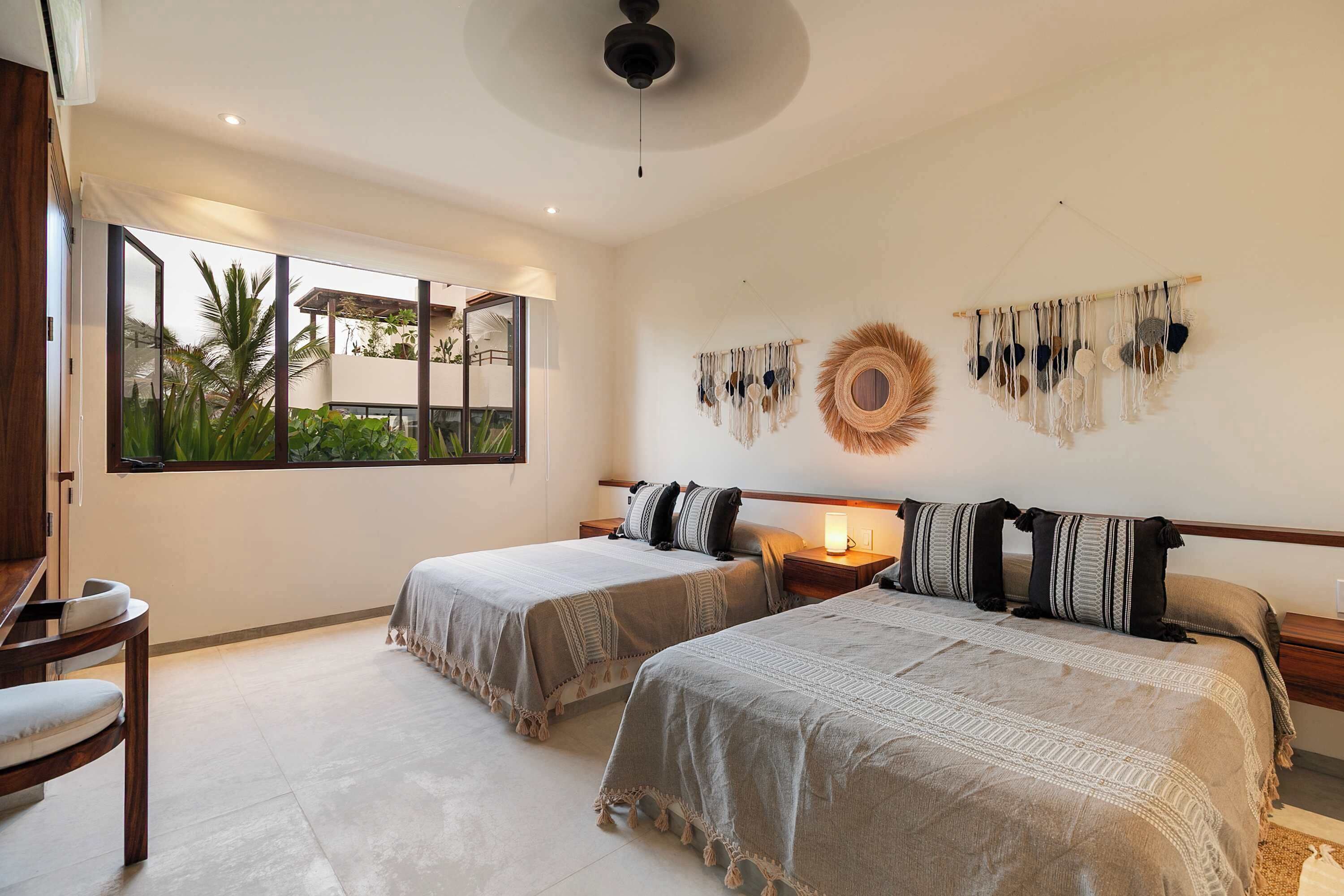 A hotel room with two beds, a large window, a ceiling fan, and wall decor.