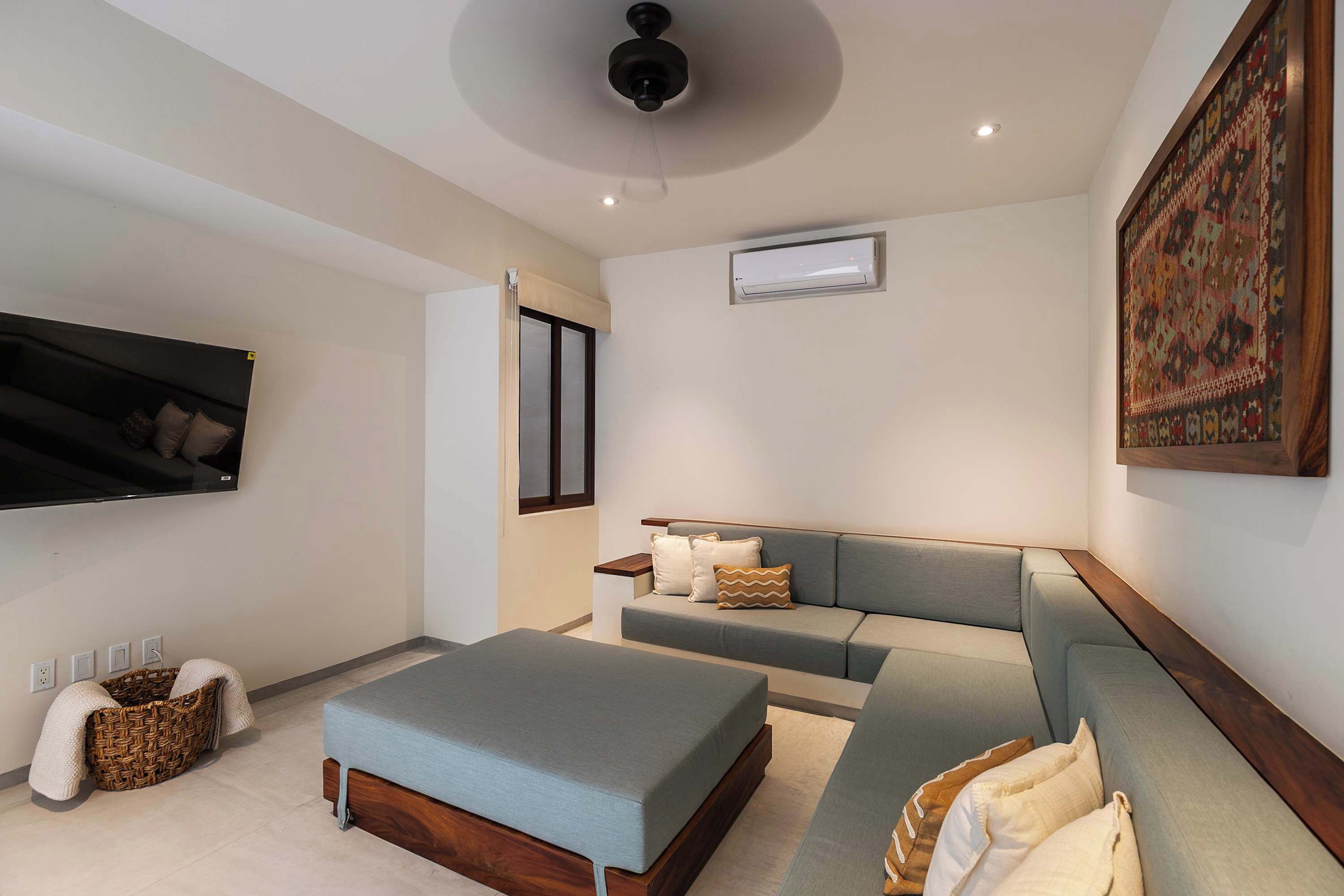 Ein modernes Wohnzimmer mit einem grauen Sofagarnitur, einem flachbildfernseher an der Wand und einem Deckenventilator.