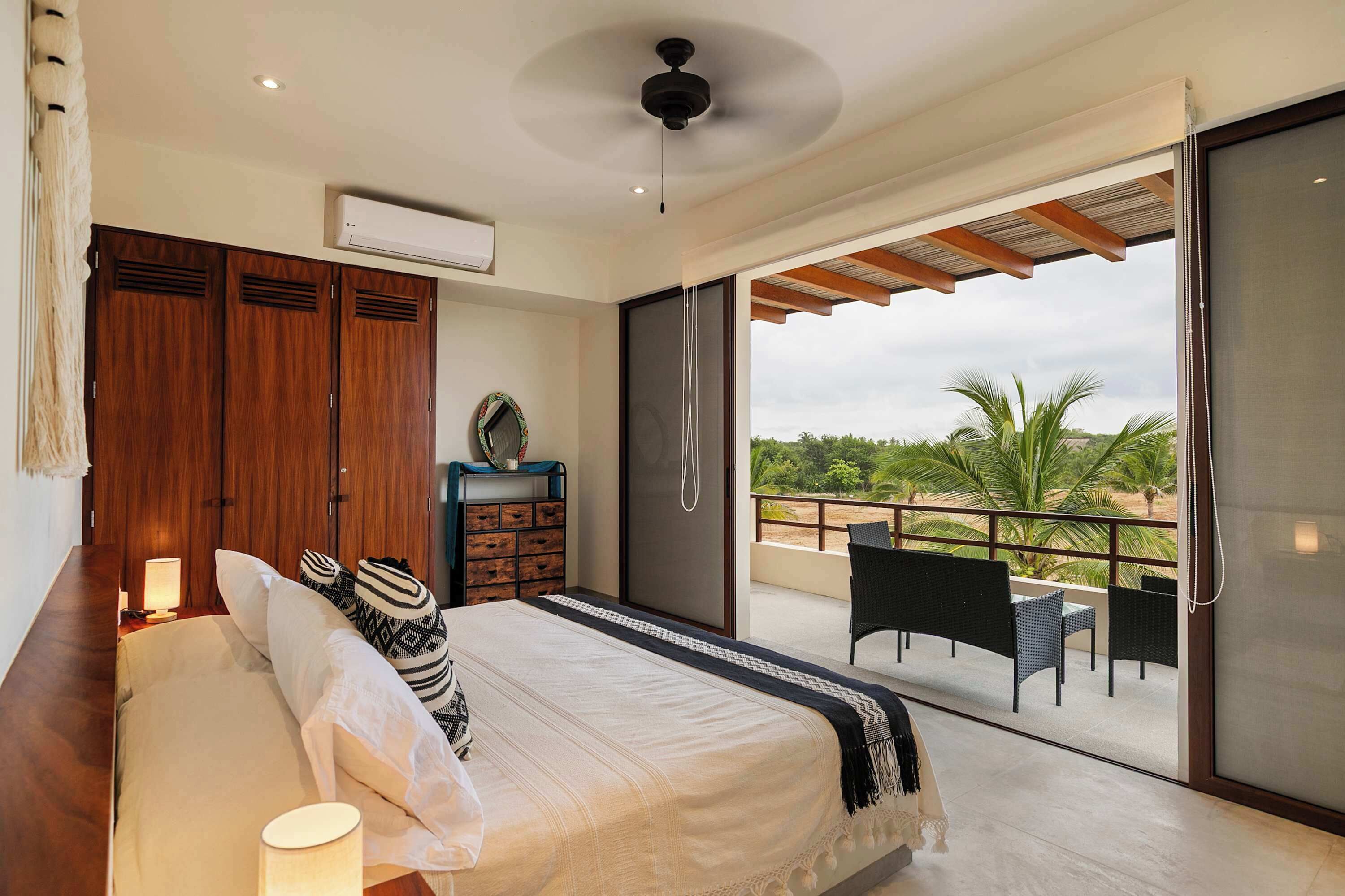 Une chambre à coucher avec un lit, une commode, un miroir et un balcon équipé de chaises.