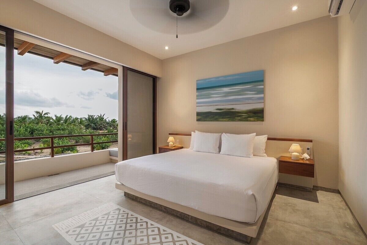 Una habitación de hotel con una cama grande, vistas a palmeras y un cuadro en la pared.