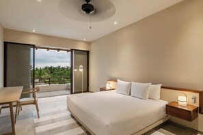 A hotel room with a bed, bedside tables, a table with chairs, and a view of greenery outside.