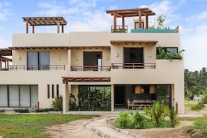 A modern two-story building with a flat roof, large windows, and a covered outdoor seating area.