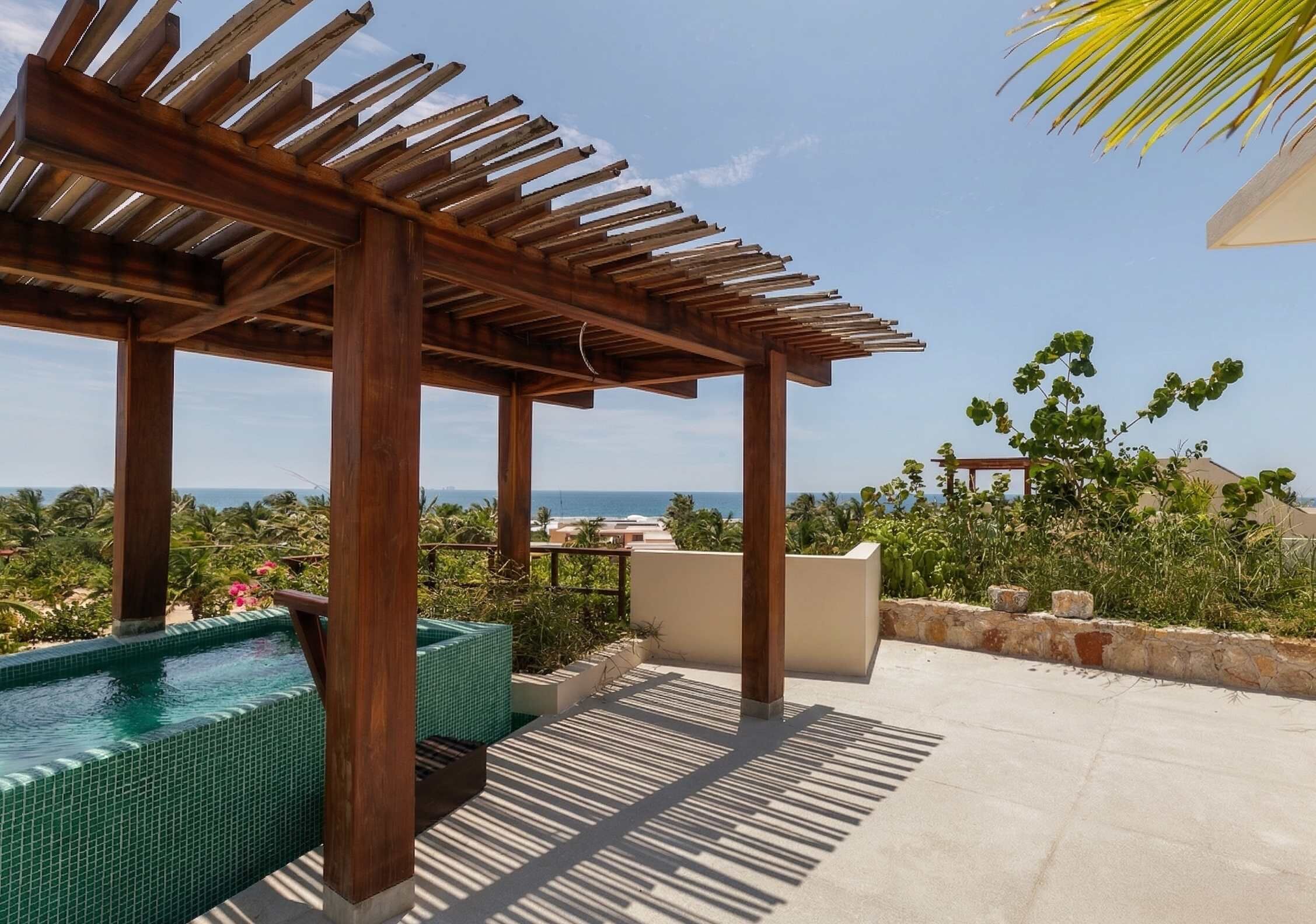 A wooden pergola with a pool and a view of the ocean.