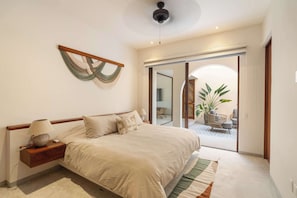 A bedroom with a bed, nightstand, lamp, and a wall-mounted decorative piece. - Private 4BR Casita | Beach Club, Pools & Padel (Zihuatanejo)