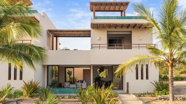 Edifici modern de dos pisos amb zona d'estar a l'exterior coberta, piscina i jardí tropical.