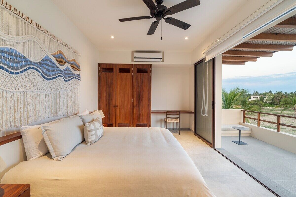 Una camera da letto con un letto, una ventola a soffitto, un'armadio in legno, una scrivania e un balcone con vista.