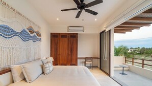 Ein Schlafzimmer mit einem Bett, Deckenventilator, Holzschrank, Schreibtisch und einem Balkon mit Blick.