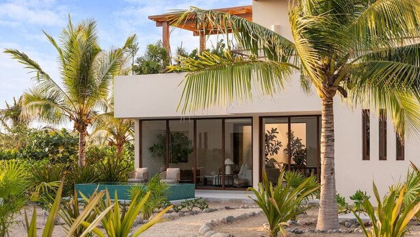 Ein modernes Haus mit überdachtem Außenbereich, umgeben von tropischen Pflanzen und einem Sandgarten.