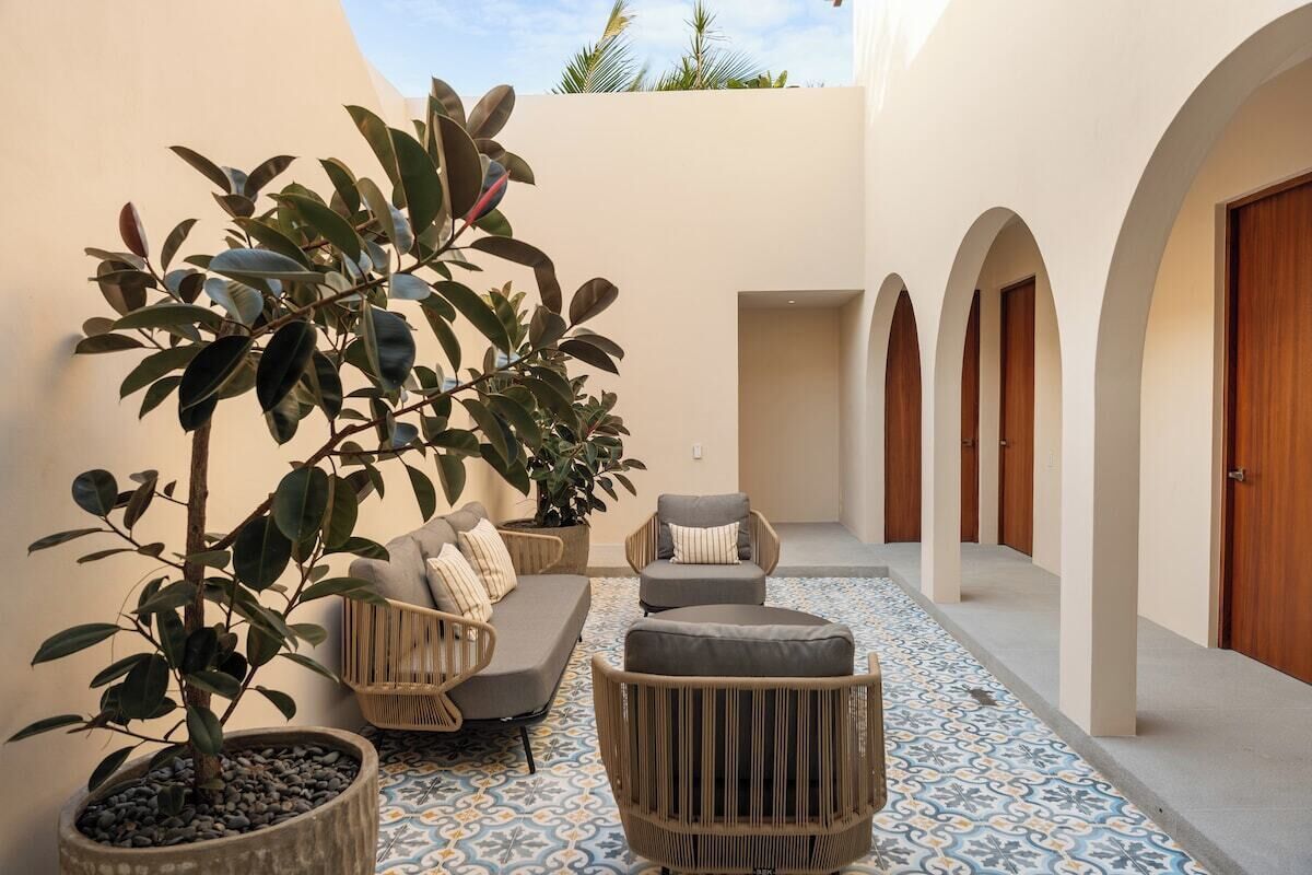 A courtyard with a sofa, chairs, potted plants, and a patterned floor.