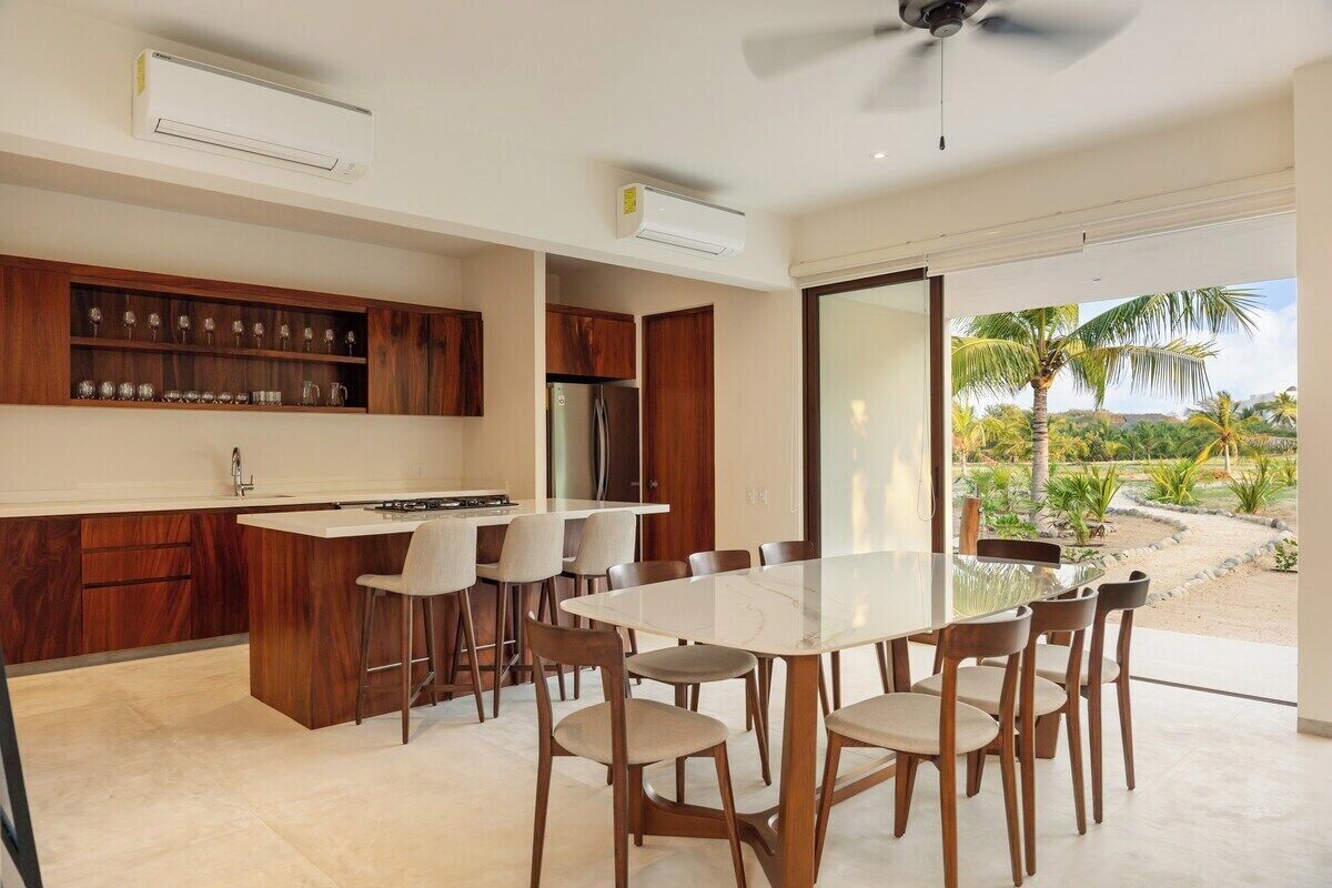 A modern kitchen with a dining area, built-in wooden cabinets, and a large glass door leading to a garden view.