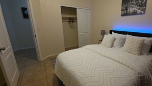 Ein Schlafzimmer mit Bett, Nachttisch, Lampe, Kleiderschrank und einem Wandbild.