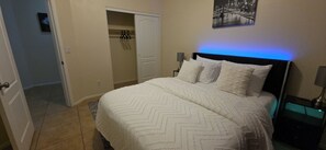 Ein Schlafzimmer mit Bett, Nachttisch, Lampe, Kleiderschrank und einem Wandbild.