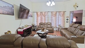 Ein Wohnzimmer mit braunen Ledersofas, einem Flachbildfernseher, einer Chandelüster und einem Essbereich mit Tisch und Stühlen.