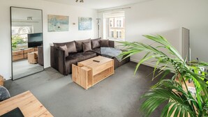 Ein modernes Wohnzimmer mit einem braunen Ledersofa, einem Holztisch, einem großen Spiegel und einer Zimmerpflanze.