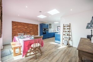 A modern kitchen with blue cabinets, a dining area with a pink tablecloth, and a wooden chair.