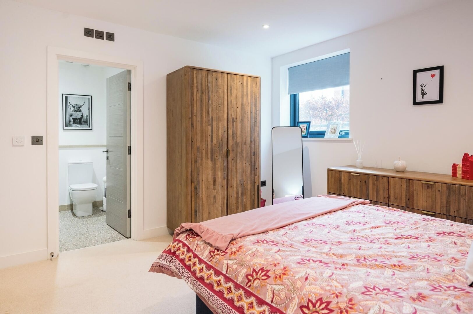 A bedroom with a bed, wooden wardrobe, a bathroom with toilet, and a window with a view.