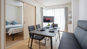 Quarto de hotel moderno com uma cama, uma mesa de jantar com cadeiras, um sofá, uma televisão de tela plana e um minibar.