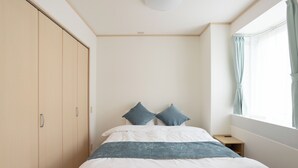 Quarto com cama, duas almofadas, mesa de cabeceira, guarda-roupa e janela com cortinas.