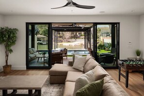 A modern living room with a sofa, coffee table, and a foosball table. - Luxury 3-Story Lakehouse |Pool + Hot Tub + Sundeck (Horseshoe Bay)